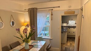 A dining area with a table set for four, a vase with flowers, and a view of the kitchen through an open door. - Spacious 3 bed holiday cottage in Hunstanton only 150 metres to the beach. (Hunstanton)