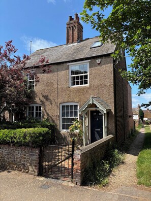 A traditional brick house with a black front door, a small porch, and a chimney.