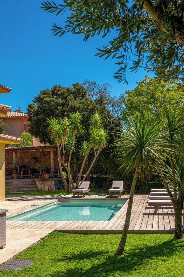 A pool area with a wooden deck, lounge chairs, and palm trees.