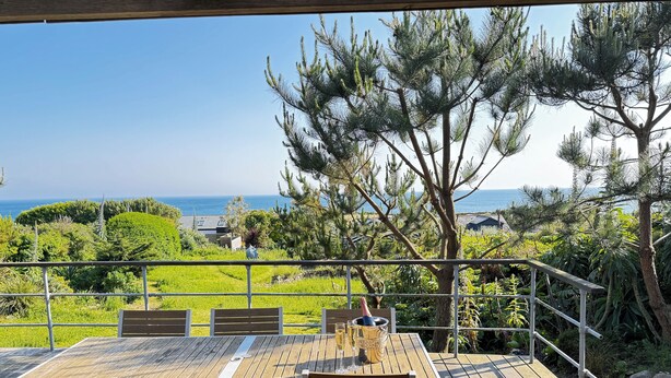 A wooden deck with a table and chairs overlooking a coastal landscape.