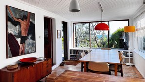 A spacious dining area with a large wooden table, modern pendant lighting, and a view of the outdoors through large windows.