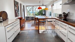A modern kitchen with white cabinetry, a wooden dining table, and a large window offering a view of the outdoors.