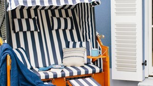 A striped beach chair with a canopy, a small table, and a bench.