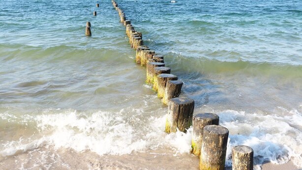 A wooden breakwater extending into the sea with waves crashing against it.
