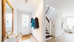 A bright hallway with a wooden floor, a white door, and a staircase leading to another room.