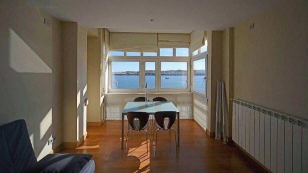 Una habitación con una mesa y sillas, vista al mar y un radiador a lo largo de la pared.