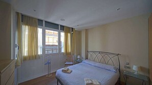Un dormitorio con una cama, un escritorio, una silla y un ventanal con cortinas.