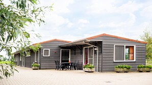 A two-story building with a covered patio area, a dining table with chairs, and potted plants. - Luxury Group accommodation in a rural area with its own outdoor area. (Rijpwetering)
