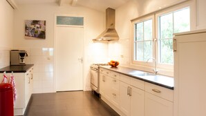 A modern kitchen with white cabinets, a stainless steel range hood, a coffee machine, and a window with a view of greenery. - Luxury Group accommodation in a rural area with its own outdoor area. (Rijpwetering)
