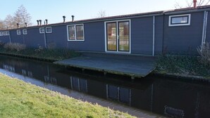 A modern building with a flat roof, large windows, and a small deck extending over a canal. - Luxury Group accommodation in a rural area with its own outdoor area. (Rijpwetering)