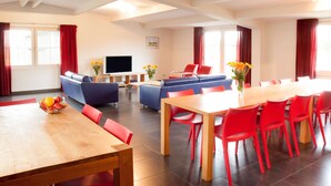 A modern hotel room with a dining area, a sofa set, a TV, and a large window with curtains. - Luxury Group accommodation in a rural area with its own outdoor area. (Rijpwetering)