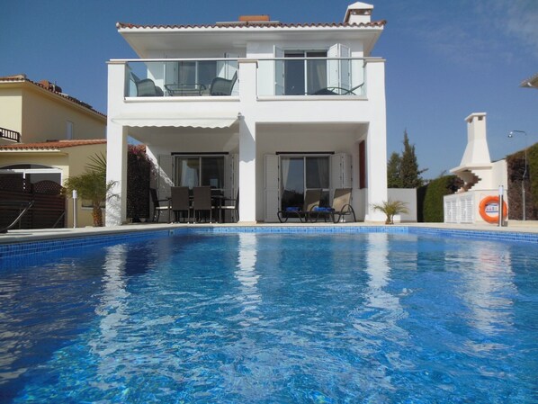 A two-story white building with a swimming pool in front.