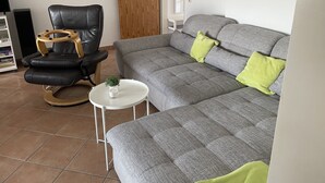 A living room with a grey sofa, a black leather chair, a small white table, and a wooden door. - Great apartment with good facilities in a prime location in Schillig (Wangerland)