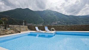 Ein Swimmingpool mit zwei Liegestühlen, einer Steinmauer und Blick auf Berge.