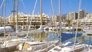 A marina with multiple boats docked, a clear sky, and buildings in the background. - SPECIAL FAMILIES, WI-FI, BEACH, POOL, SPORTS TRACKS (Málaga, Benalmádena)