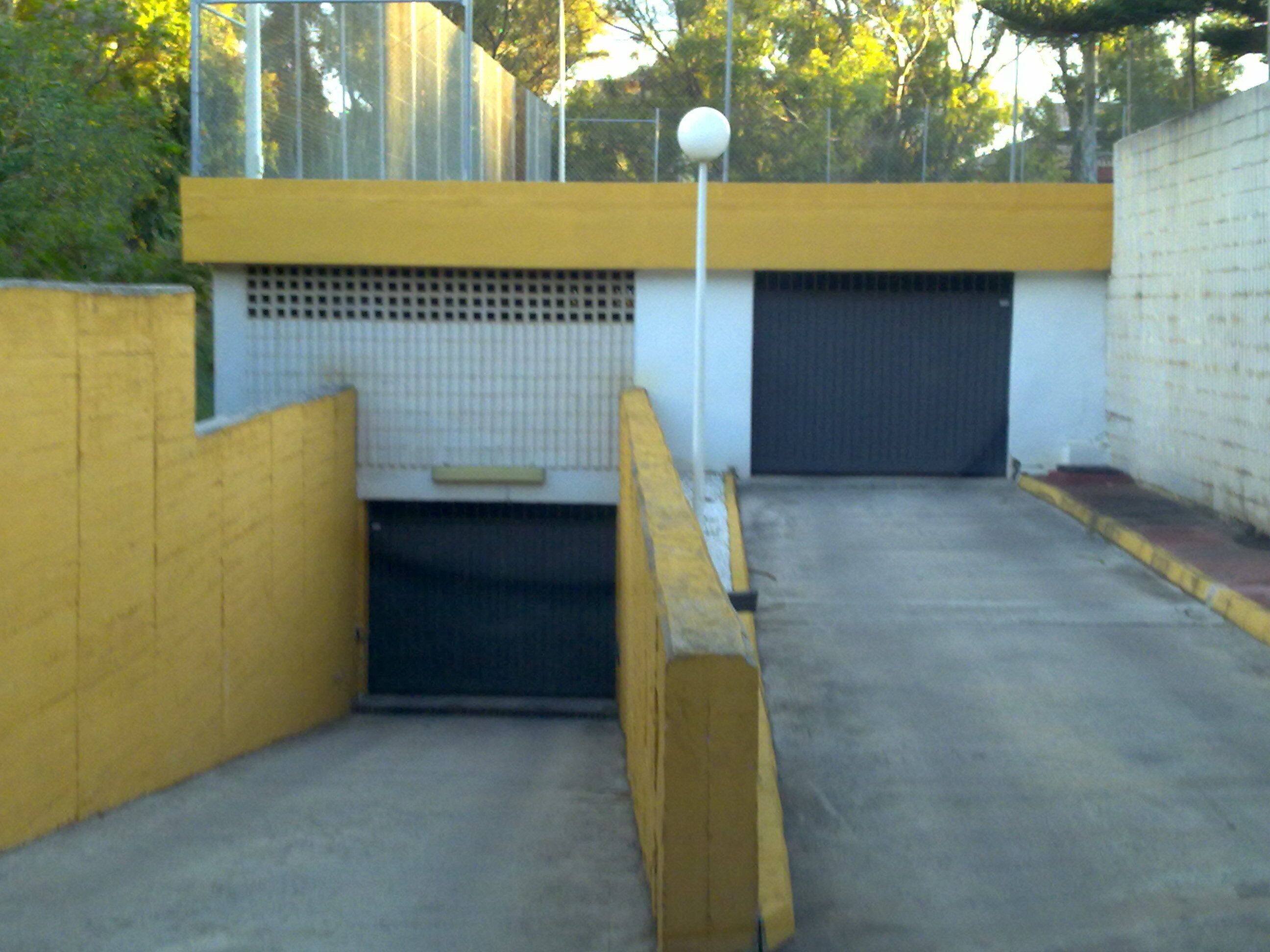 Un estacionamiento con paredes amarillas, una cerca metálica y una puerta de garaje cerrada.