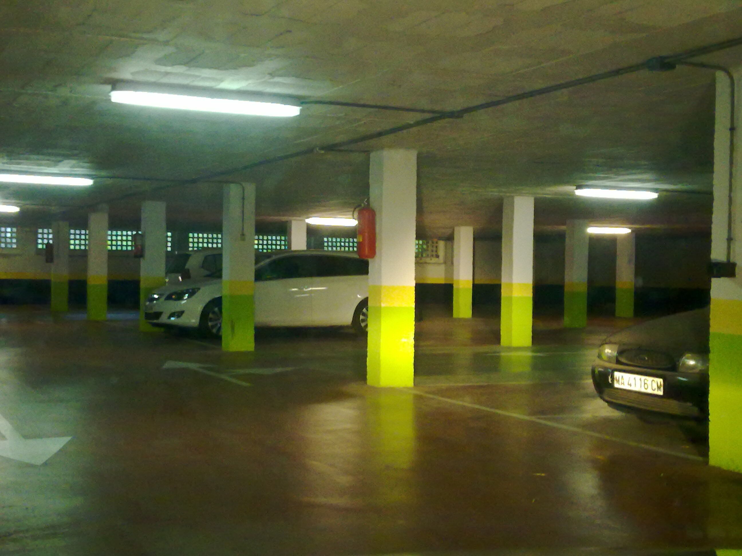 Useita kerroksia sisältävä pysäköintihalli, jossa on betonipilarit ja loisteputkivalaistus.