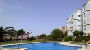 A swimming pool surrounded by a grassy area with a building in the background. - SPECIAL FAMILIES, WI-FI, BEACH, POOL, SPORTS TRACKS (Málaga, Benalmádena)