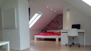 A modern loft bedroom with a sloped ceiling, a skylight, a bed with a red patterned blanket, a white desk with a chair, and a brick accent wall. - in a good location to Dusseldorf and Cologne and the JEVER Skihalle Neuss (Grevenbroich)