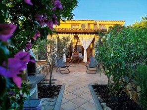 A patio area with a yellow building, outdoor seating, and a garden.