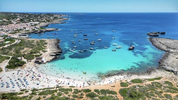 An aerial view of a coastal town with a beach, boats, and rocky terrain. - Stylish, spacious and airy, in a quiet area  but close to beach, restos & shops (Sant Lluís)