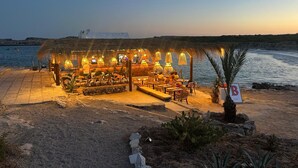 A beachside restaurant with outdoor seating, a thatched roof, and a view of the sea. - Stylish, spacious and airy, in a quiet area  but close to beach, restos & shops (Sant Lluís)