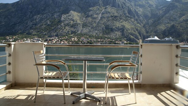 A balcony with a table and chairs overlooking a mountainous landscape. - Immaculate Apartment,  Uninterrupted Stunning Bay Views , Private parking (Kotor)