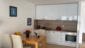 A modern kitchen with white cabinets, a wooden countertop, and a dining area with a wooden table and chairs. - Immaculate Apartment,  Uninterrupted Stunning Bay Views , Private parking (Kotor)