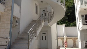 A white building with a curved staircase, a door at the bottom, and a person in a pink dress walking away. - Immaculate Apartment,  Uninterrupted Stunning Bay Views , Private parking (Kotor)