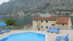 A swimming pool with blue chairs and a view of a mountain and a cruise ship in the background. - Immaculate Apartment,  Uninterrupted Stunning Bay Views , Private parking (Kotor)