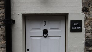 A white door with the number 1, a black doorbell, and a sign reading "THE BOBBIN" on a stone wall.