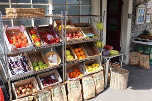 A produce stand with baskets of fruits and vegetables, including tomatoes, apples, and oranges, and bags of selected potatoes. - Style and Comfort - Welcome to The Bobbin (Ashford in the Water)