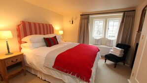 A neatly made bed with a striped headboard, a bedside lamp, and a chair with folded towels.