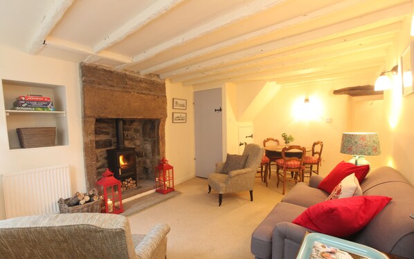 A cozy living room with a stone fireplace, a dining area with a table and chairs, and a sofa with red cushions. - Style and Comfort - Welcome to The Bobbin (Ashford in the Water)