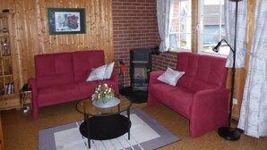 A cozy living room with two red sofas, a glass coffee table, a fireplace, and a large window with curtains. - The house is located right on the edge of the Müritz National Park (Userin)
