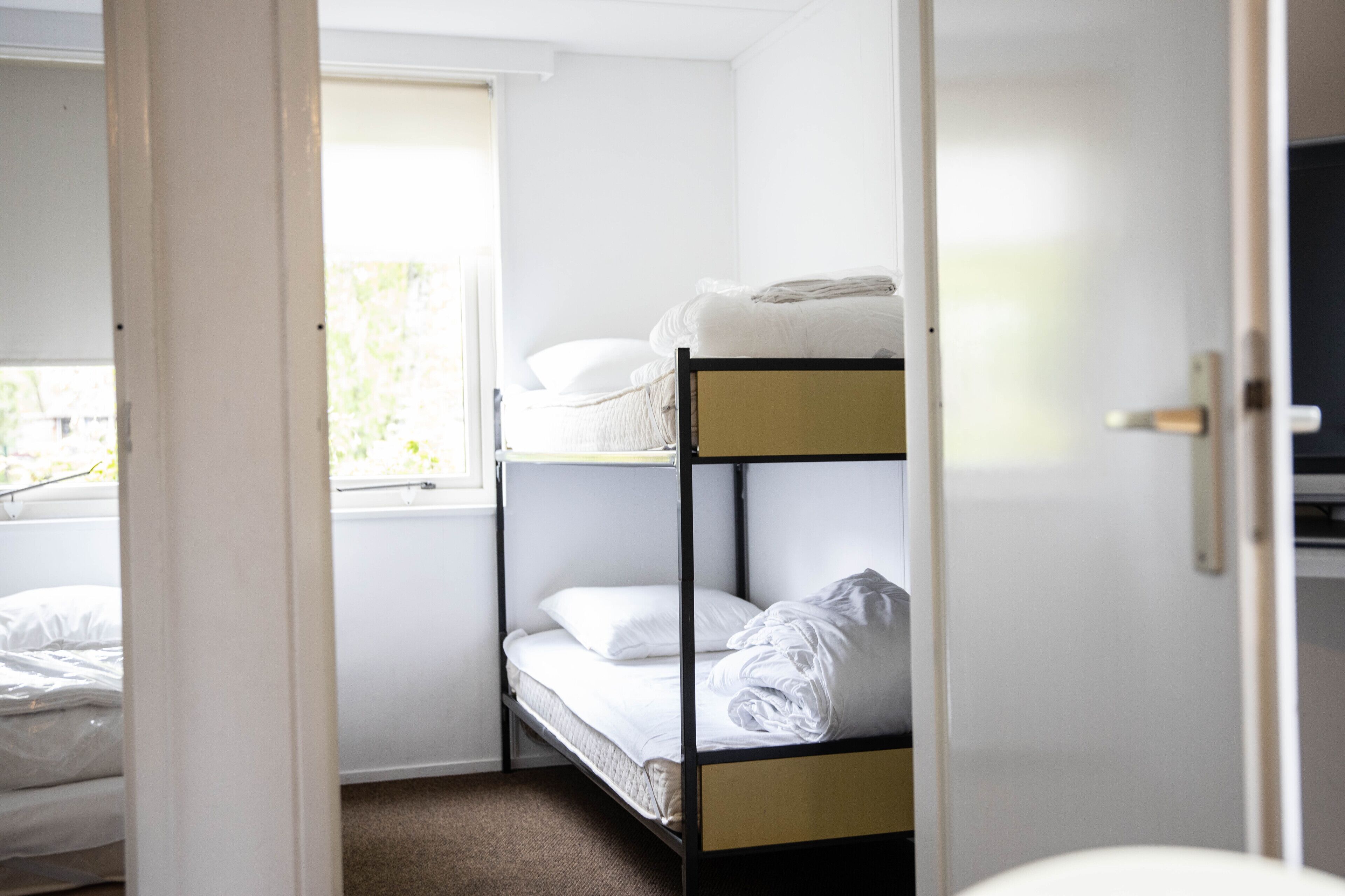 Une chambre avec un lit superposé, du linge de lit blanc et une fenêtre.