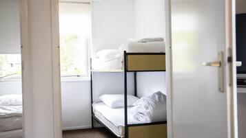 Une chambre avec un lit superposé, du linge de lit blanc et une fenêtre.