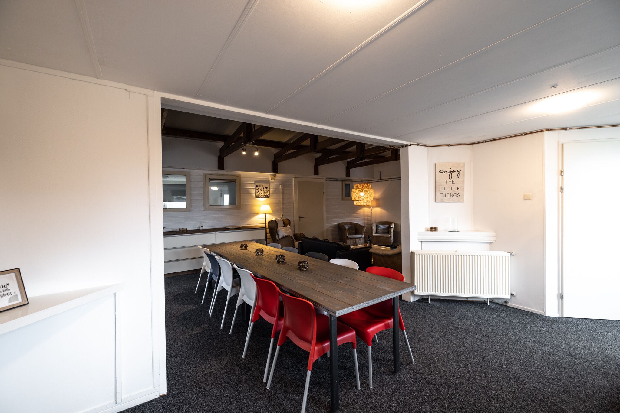 Une cuisine moderne avec des armoires blanches, un plan de travail en bois et un four encastré. On y trouve également un coin repas avec une longue table et des chaises rouges.