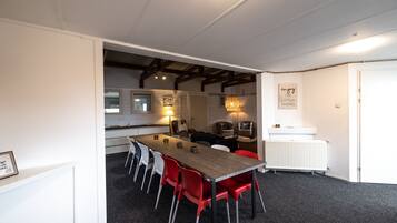 Une cuisine moderne avec des armoires blanches, un plan de travail en bois et un four encastré. On y trouve également un coin repas avec une longue table et des chaises rouges.