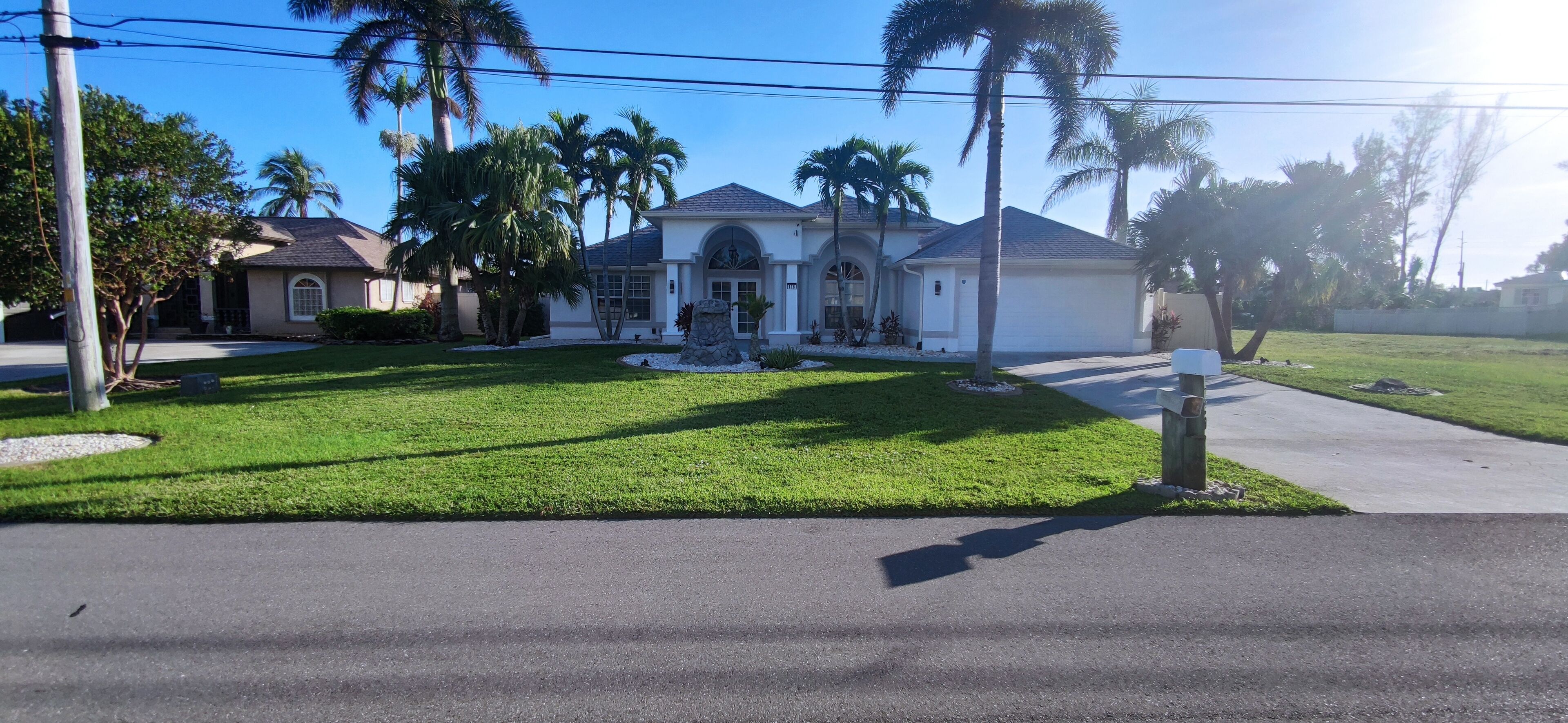 A residential house with a well-maintained lawn, palm trees, and a driveway.