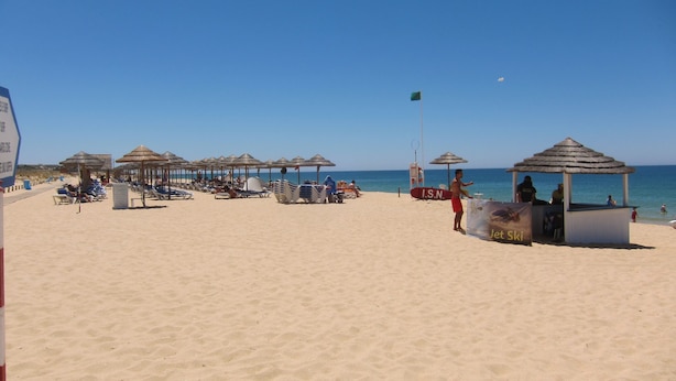 A beach with sun umbrellas, lounge chairs, and a lifeguard station.