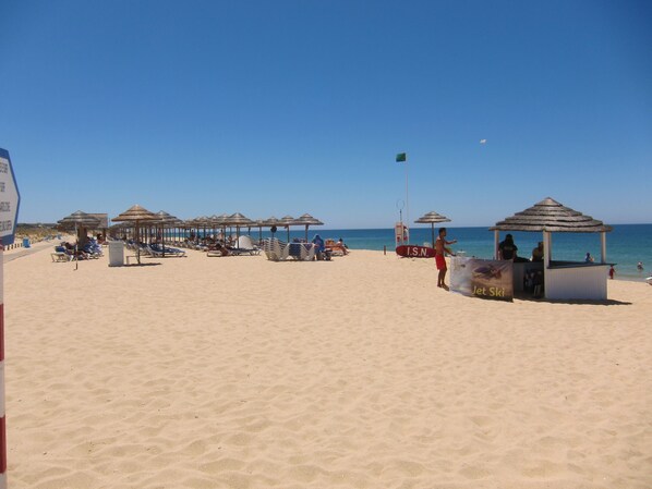 Una playa con sombrillas, sillas de descanso y una estación de salvavidas.