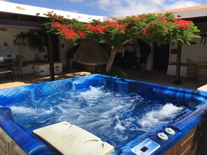 A hot tub with a control panel, surrounded by a patio area with chairs and a table.