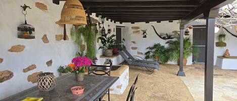Une terrasse couverte avec une table, des chaises, des plantes suspendues et une lanterne suspendue.