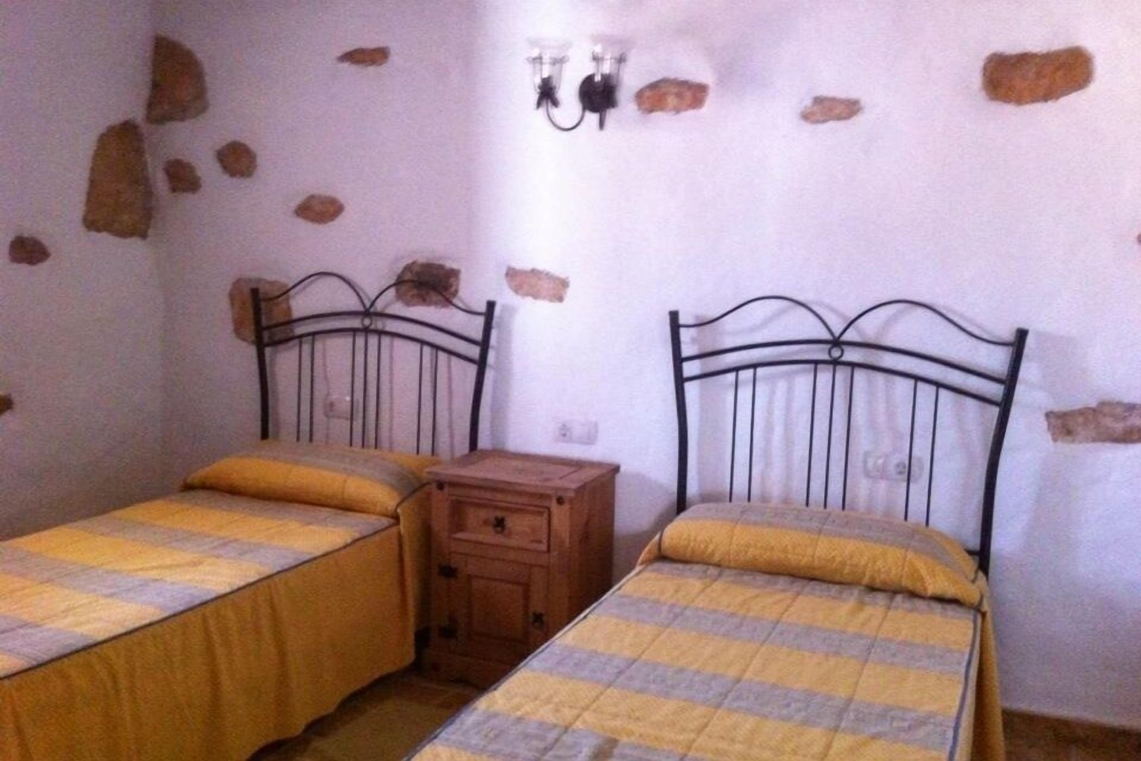 A room with two beds, each with a wooden nightstand, a stone wall, and a wall-mounted light fixture.