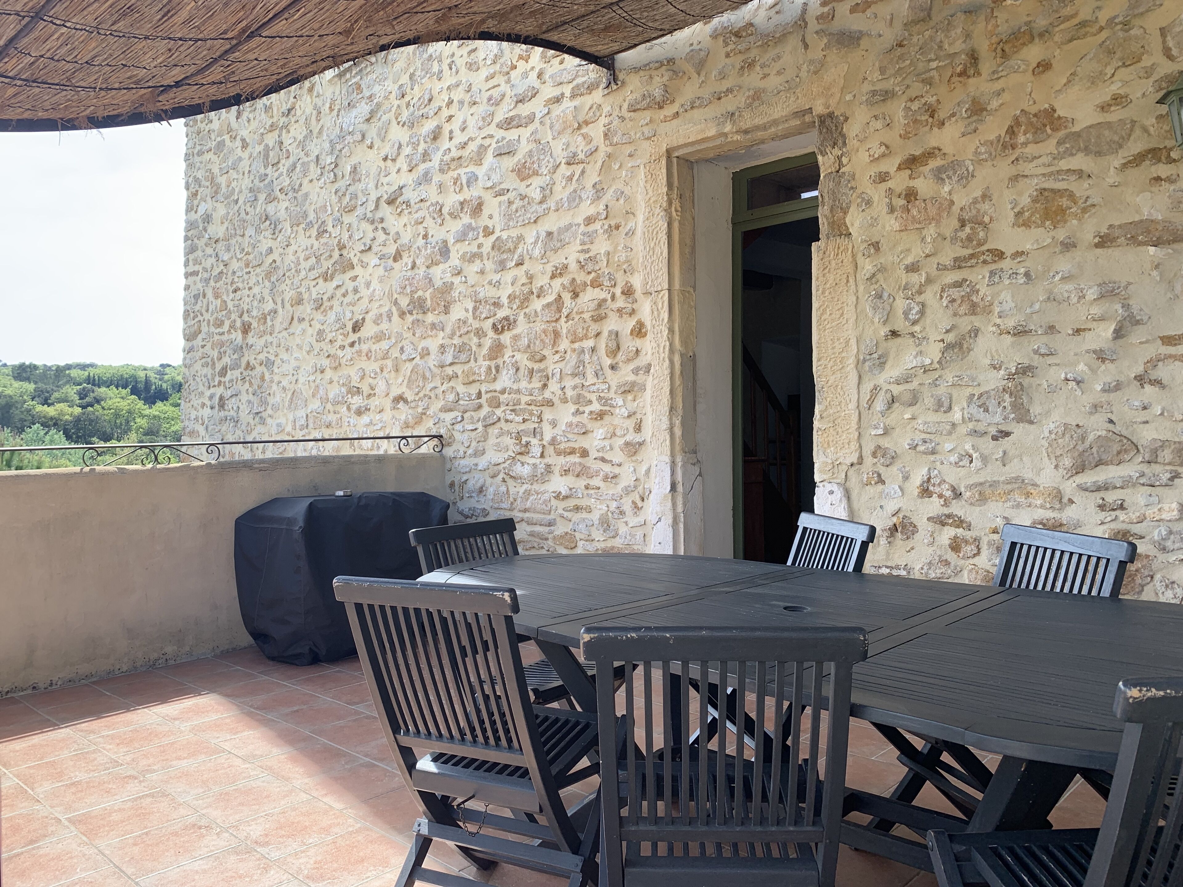 Une terrasse en pierre avec une table et des chaises, un barbecue et une vue sur la verdure.
