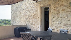 A stone wall patio with a table and chairs, a grill, and a view of greenery. - Character house, Mas du 17è,quiet,private pool 9x4,5m,air-conditioned,near Uzes (Le Pin)