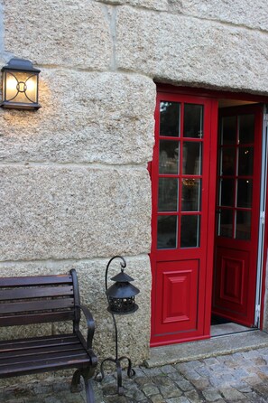 Un bâtiment en pierre avec une porte rouge et un banc à l’extérieur.