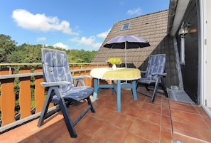 Une terrasse avec deux chaises et une table, une nappe jaune et un parasol bleu.