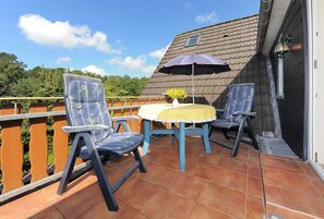 A patio with two chairs and a table, a yellow tablecloth, and a blue umbrella. - Apartment - Ferienhaus Zur Schmiede (Dunum)